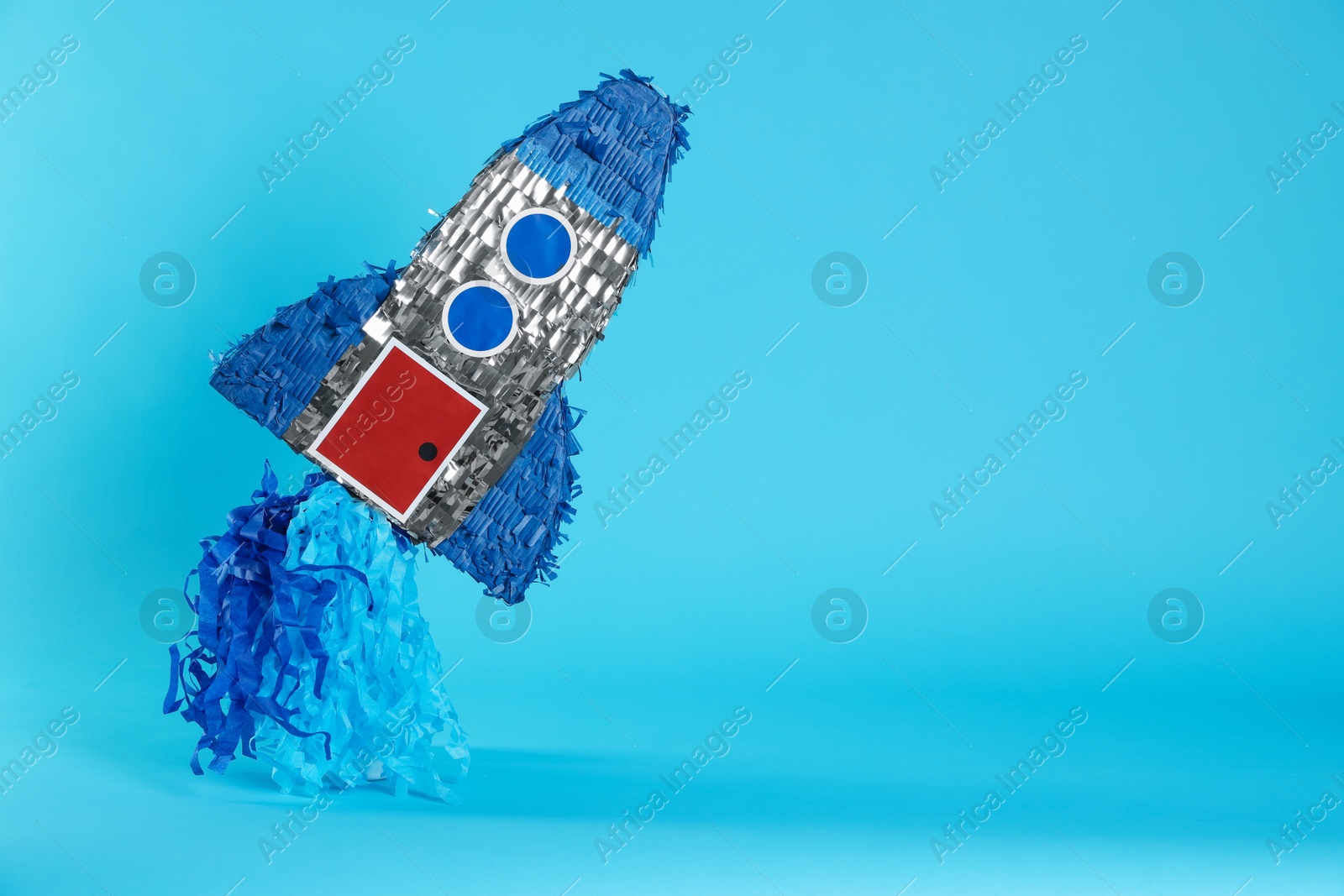 Photo of Rocket shaped pinata on light blue background, space for text