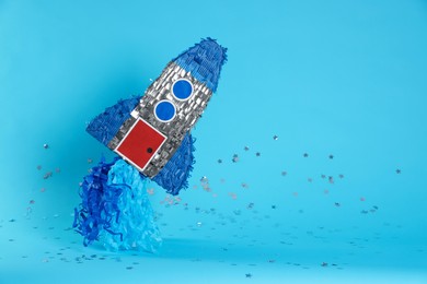 Photo of Rocket shaped pinata and confetti on light blue background, space for text