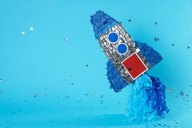 Photo of Rocket shaped pinata and confetti on light blue background, space for text