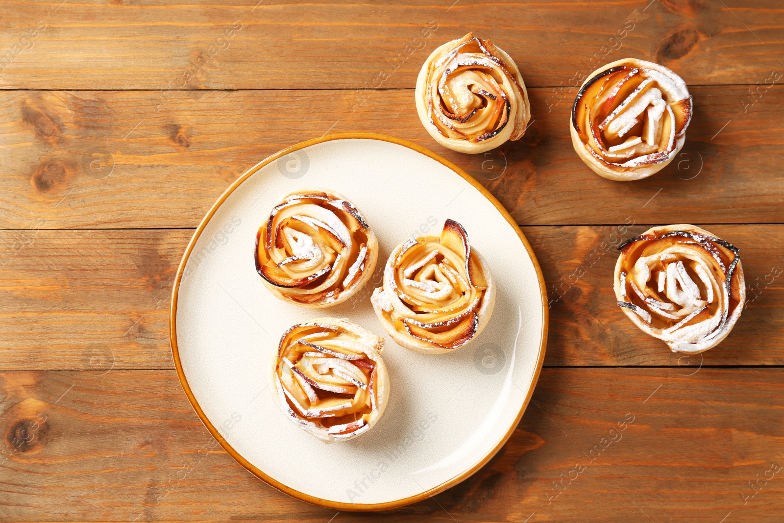 Photo of Tasty apple roses with powdered sugar on wooden table, flat lay
