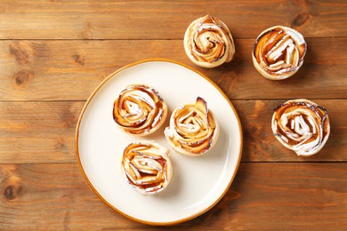 Photo of Tasty apple roses with powdered sugar on wooden table, flat lay