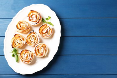 Photo of Tasty apple roses with powdered sugar served on blue wooden table, top view