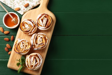 Photo of Tasty apple roses with powdered sugar served on green wooden table, flat lay. Space for text
