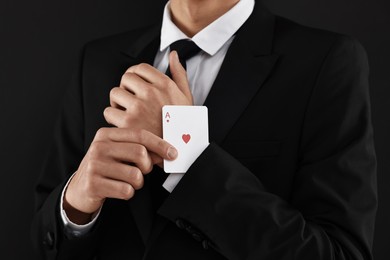 Photo of Illusionist taking playing card out of sleeve on black background, closeup