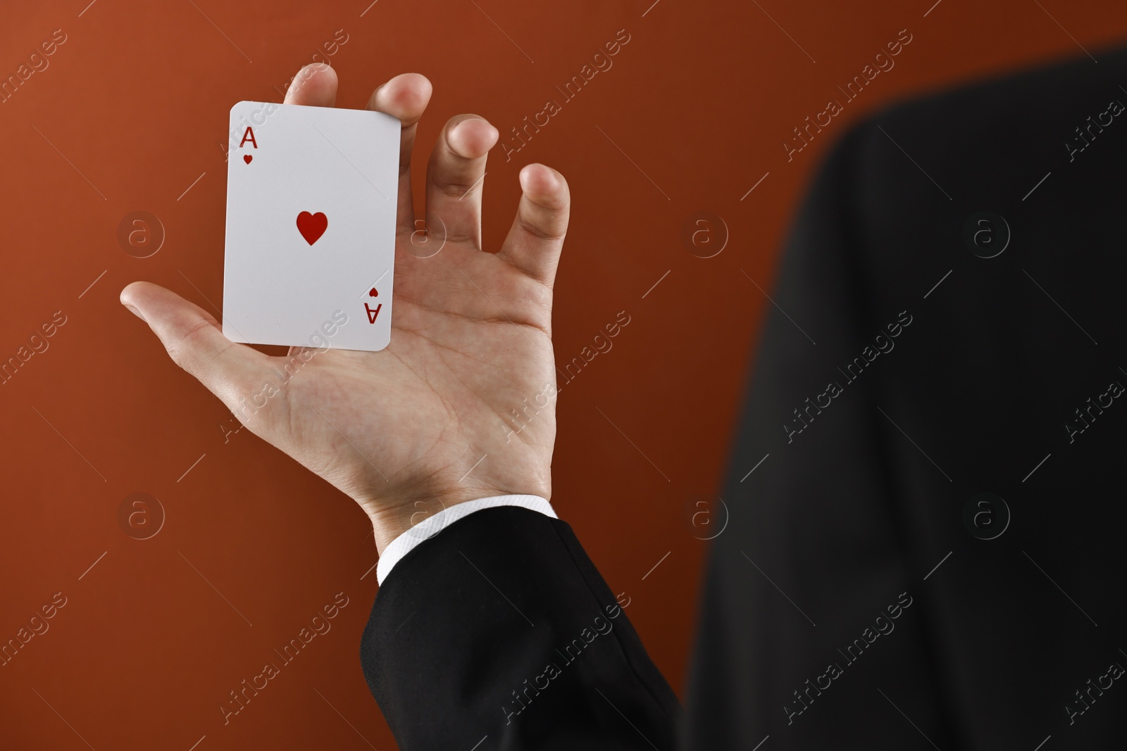 Photo of Illusionist showing playing card on dark orange background, closeup