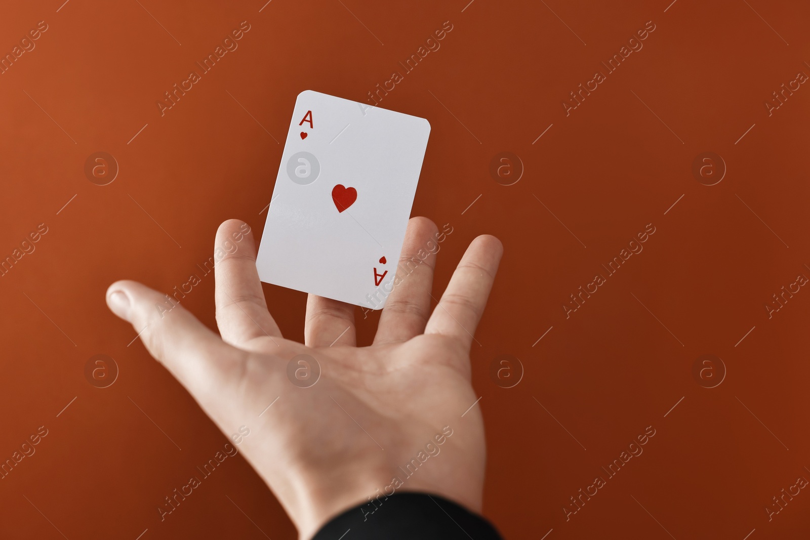 Photo of Illusionist showing playing card on dark orange background, closeup. Space for text