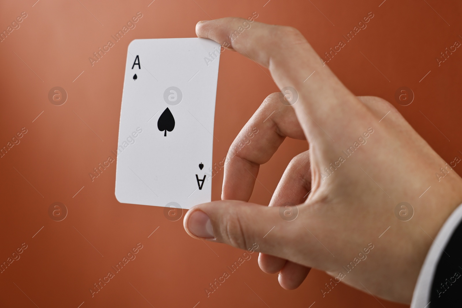 Photo of Illusionist showing playing card on dark orange background, closeup