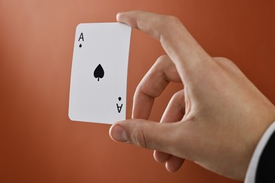 Photo of Illusionist showing playing card on dark orange background, closeup