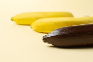 Photo of Stop racism. One dark banana and yellow ones on beige background, closeup