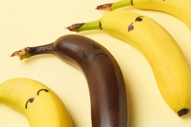 Photo of Stop racism. One dark banana among yellow ones on beige background, closeup