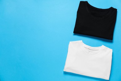 Photo of Blank t-shirts for branding on light blue background, flat lay. Mockup for design