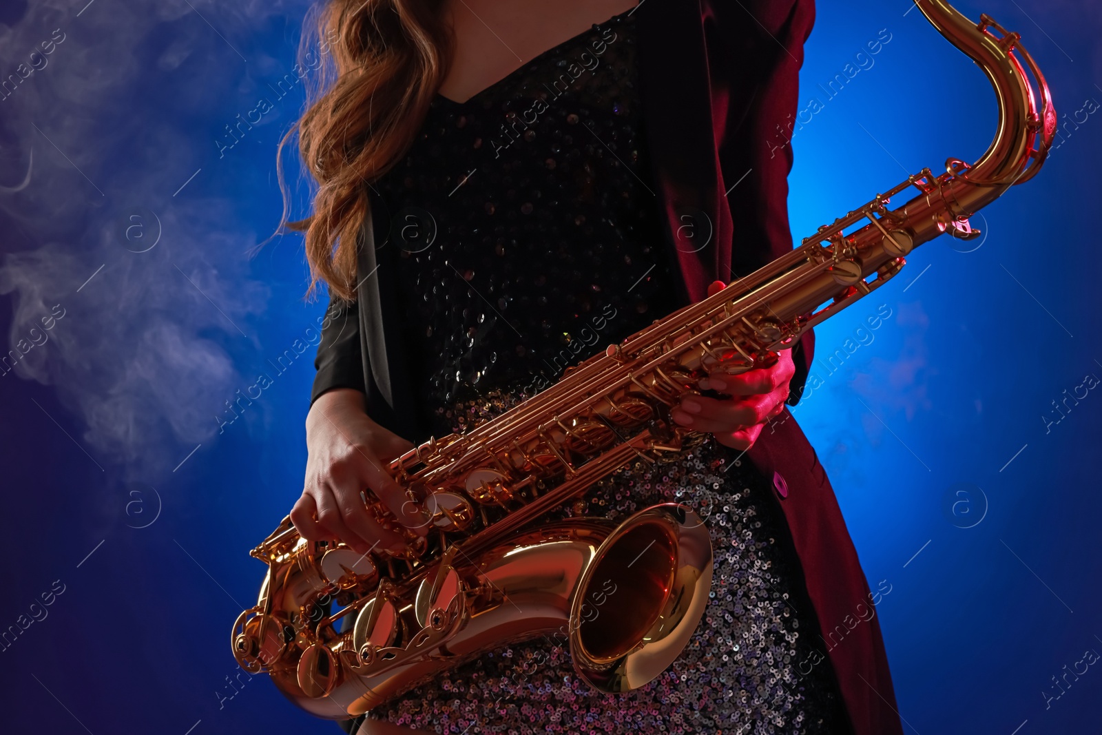 Photo of Professional musician playing saxophone on color background with smoke, closeup