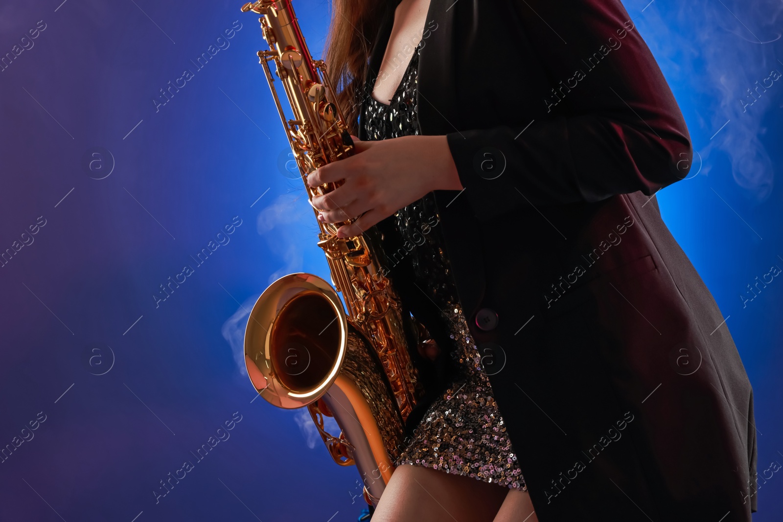 Photo of Professional musician playing saxophone on color background with smoke, closeup