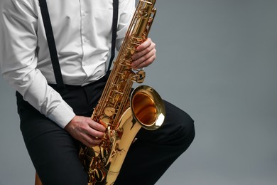 Photo of Professional musician playing saxophone on grey background, closeup. Space for text