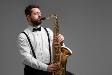 Photo of Professional musician playing saxophone on grey background. Space for text