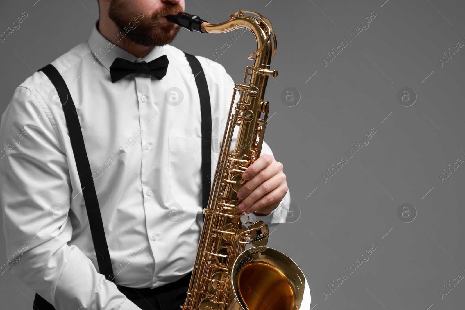 Photo of Professional musician playing saxophone on grey background, closeup. Space for text