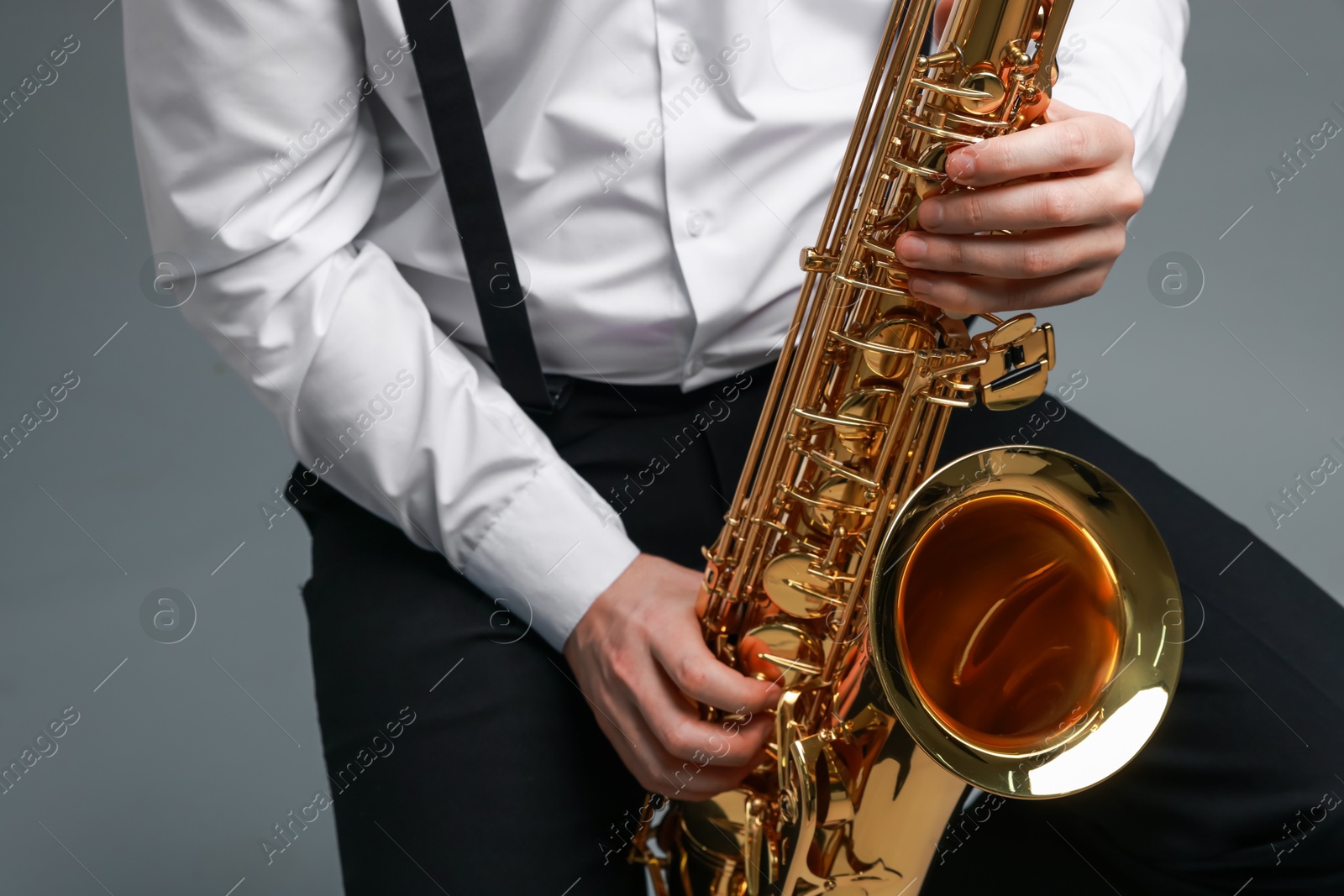 Photo of Professional musician playing saxophone on grey background, closeup