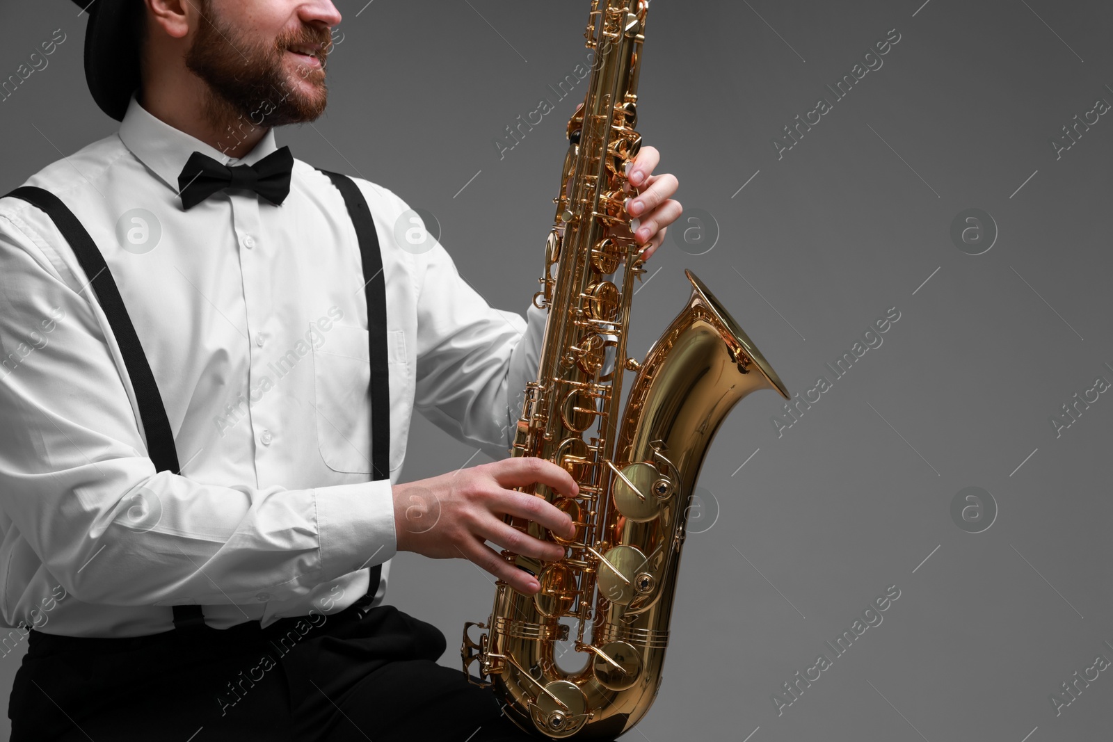 Photo of Professional musician with saxophone on grey background, closeup. Space for text