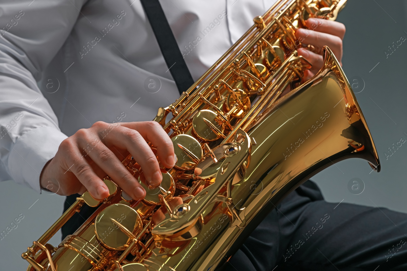 Photo of Professional musician playing saxophone on grey background, closeup