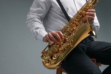 Photo of Professional musician playing saxophone on grey background, closeup