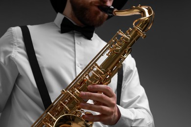 Photo of Professional musician playing saxophone on grey background, closeup