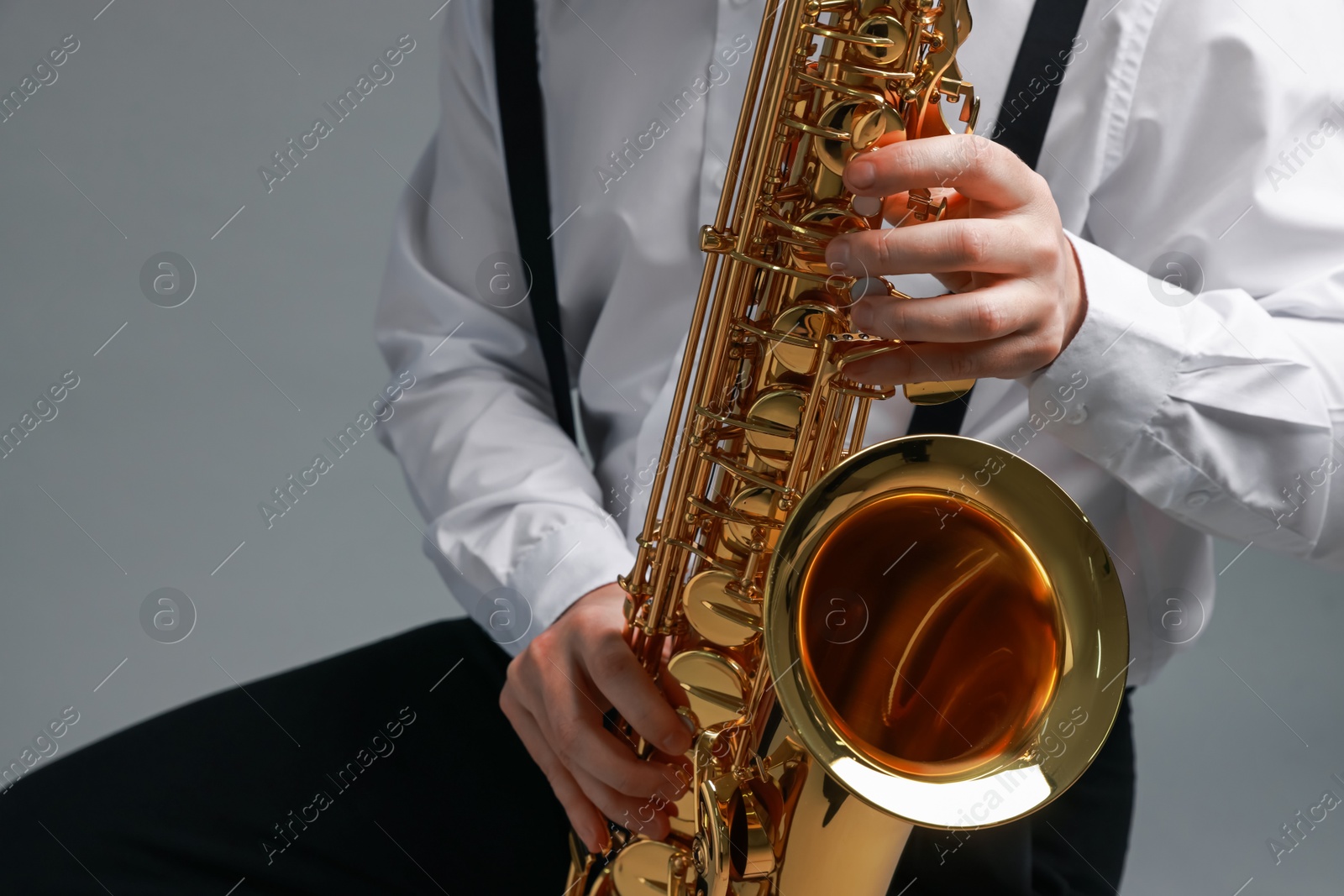 Photo of Professional musician playing saxophone on grey background, closeup