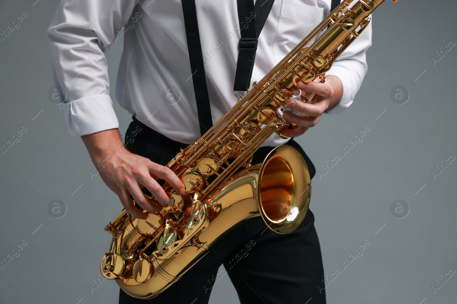 Photo of Professional musician playing saxophone on grey background, closeup