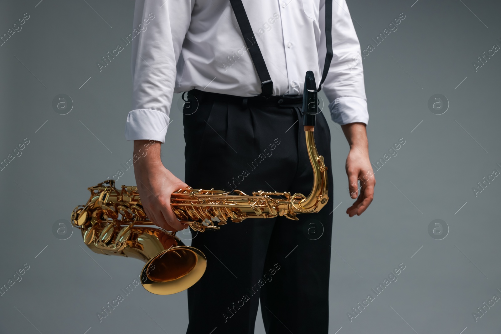 Photo of Professional musician with saxophone on grey background, closeup