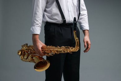 Photo of Professional musician with saxophone on grey background, closeup