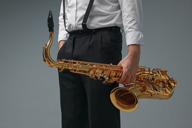 Photo of Professional musician with saxophone on grey background, closeup