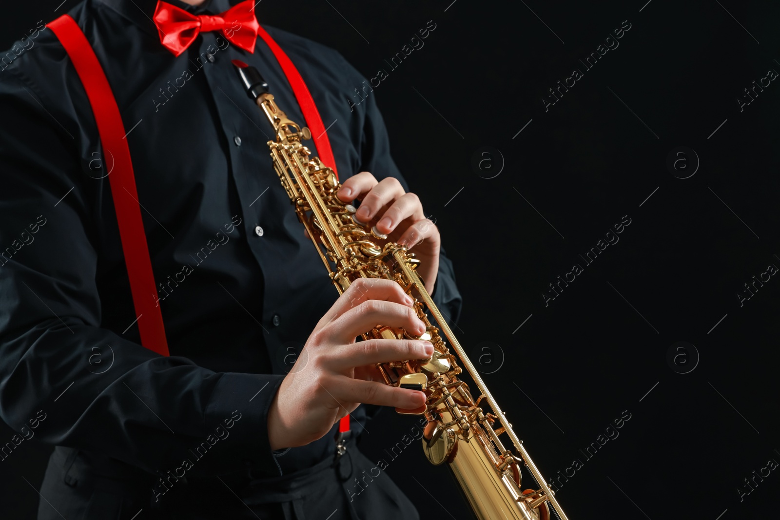 Photo of Professional musician playing soprano saxophone on black background, closeup. Space for text