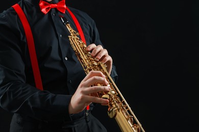 Photo of Professional musician playing soprano saxophone on black background, closeup. Space for text