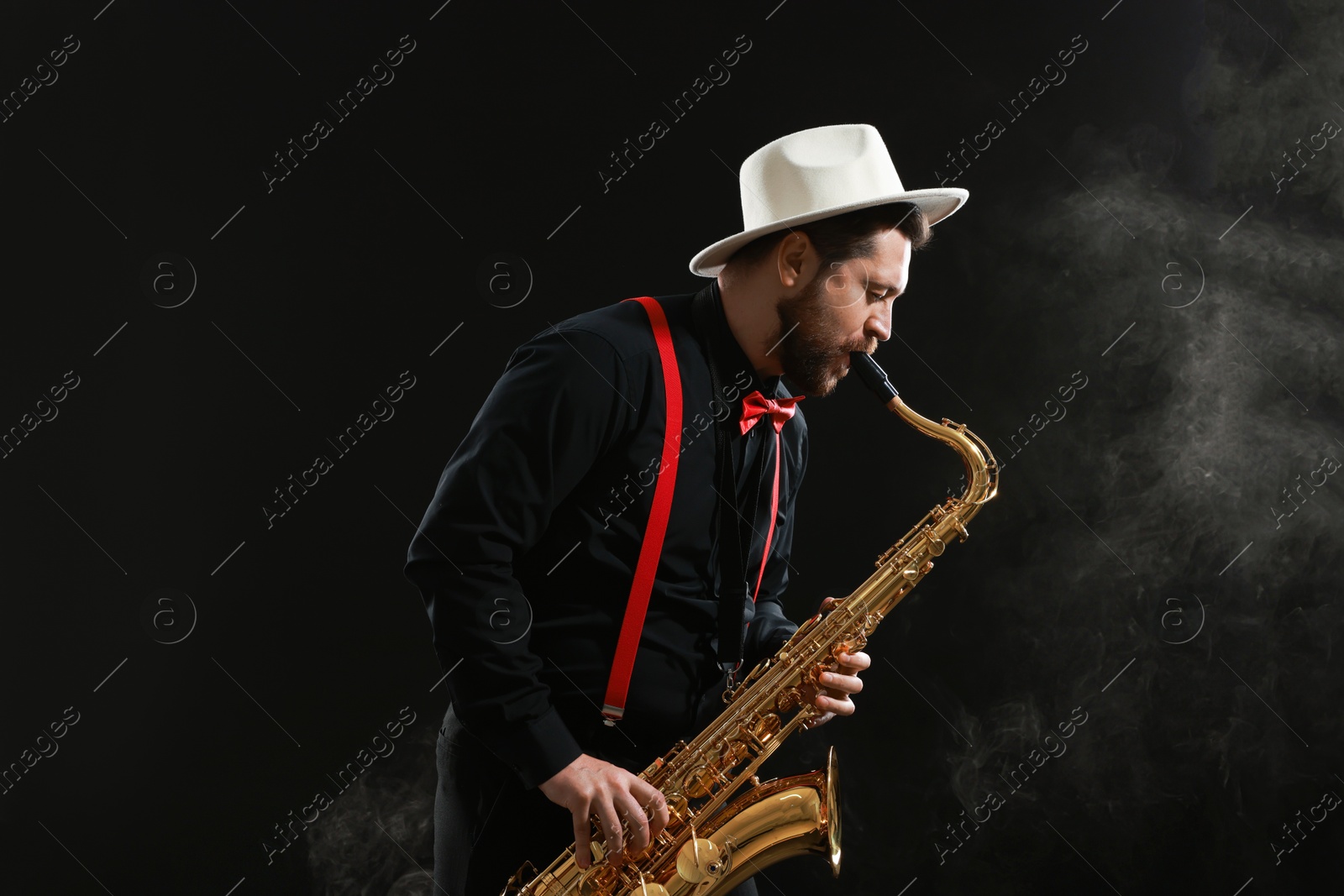 Photo of Professional musician playing saxophone on black background with smoke