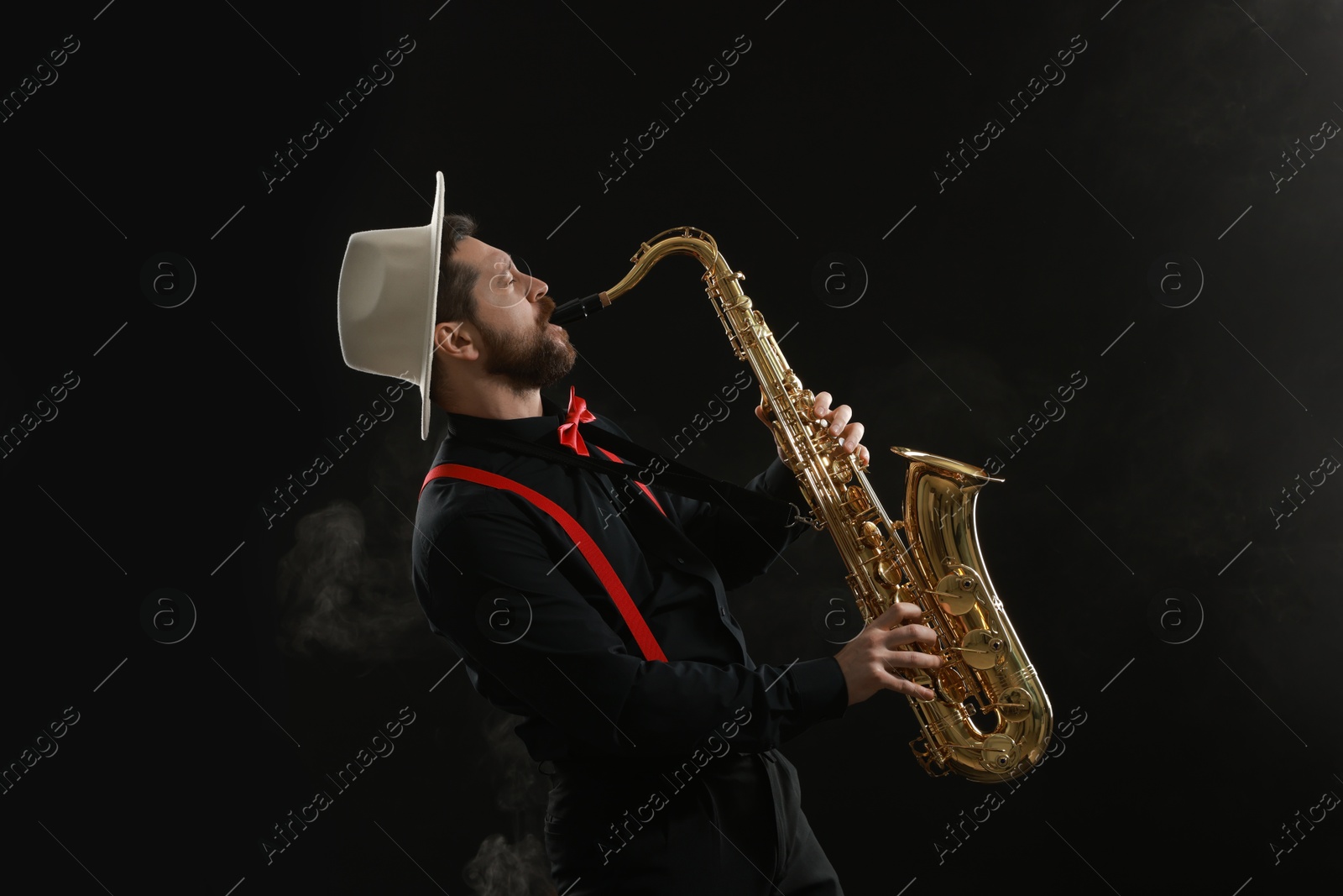 Photo of Professional musician playing saxophone on black background with smoke