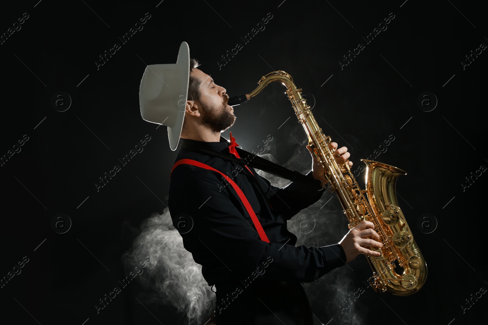 Photo of Professional musician playing saxophone on black background with smoke