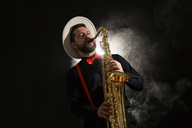 Photo of Professional musician playing saxophone on black background with smoke