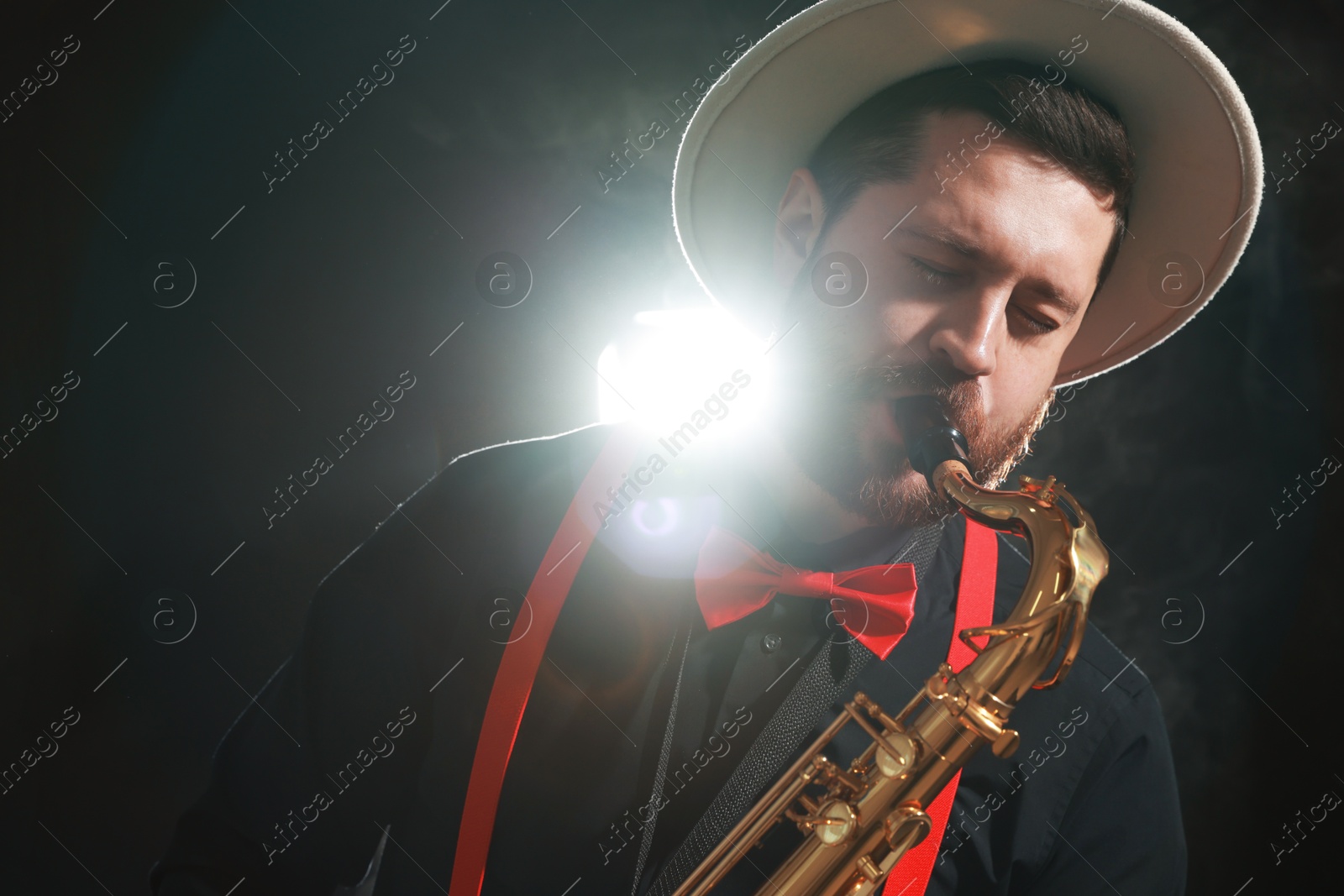 Photo of Professional musician playing saxophone on black background with smoke