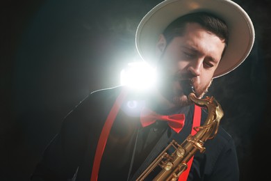 Photo of Professional musician playing saxophone on black background with smoke