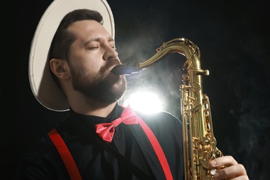 Photo of Professional musician playing saxophone on black background with smoke