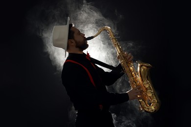 Photo of Professional musician playing saxophone on black background with smoke