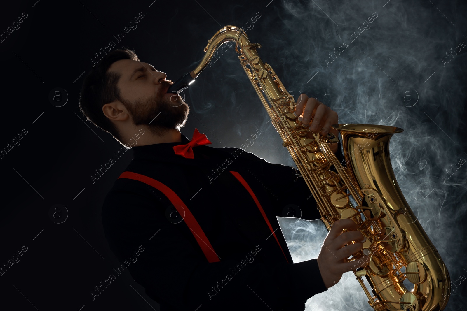 Photo of Professional musician playing saxophone on black background with smoke