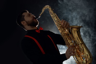 Professional musician playing saxophone on black background with smoke