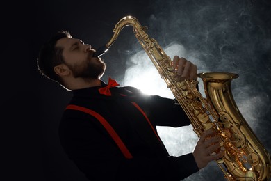 Professional musician playing saxophone on black background with smoke