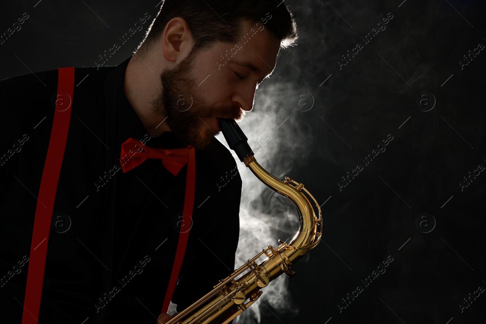 Photo of Professional musician playing saxophone on black background with smoke