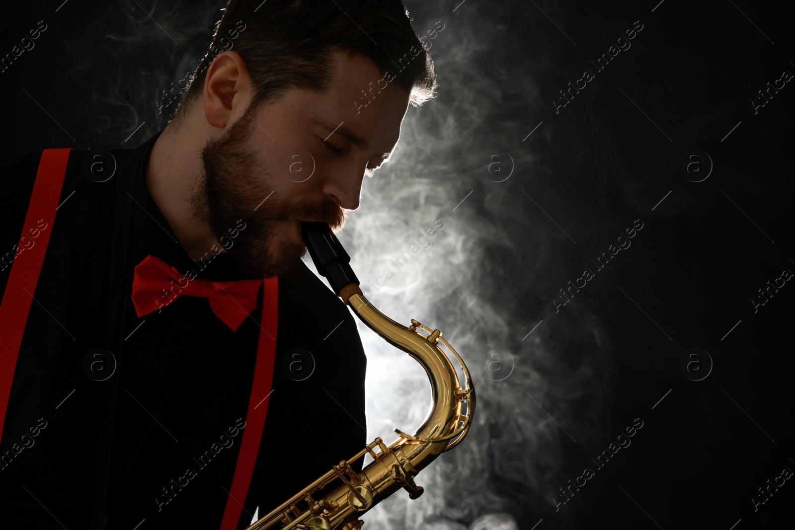 Photo of Professional musician playing saxophone on black background with smoke