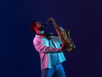 Photo of Professional musician playing saxophone on color background with neon lights