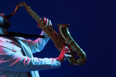 Photo of Professional musician playing saxophone on color background with neon lights, closeup