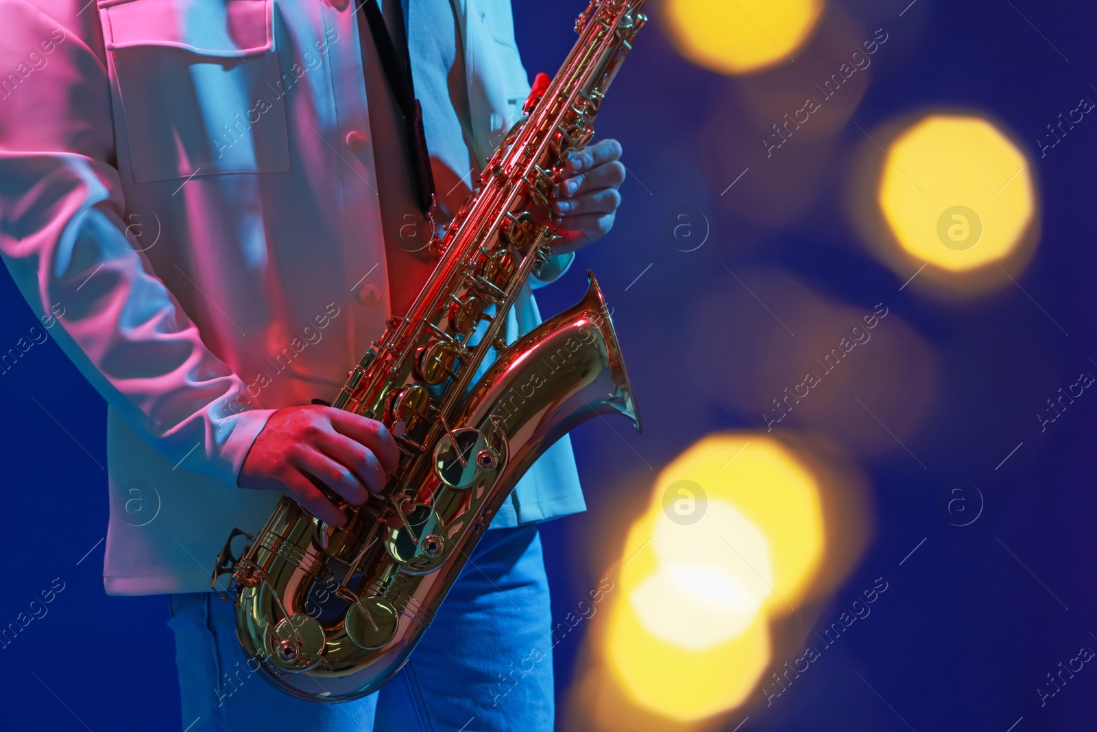 Photo of Professional musician playing saxophone on blue background with blurred lights, closeup. Bokeh effect