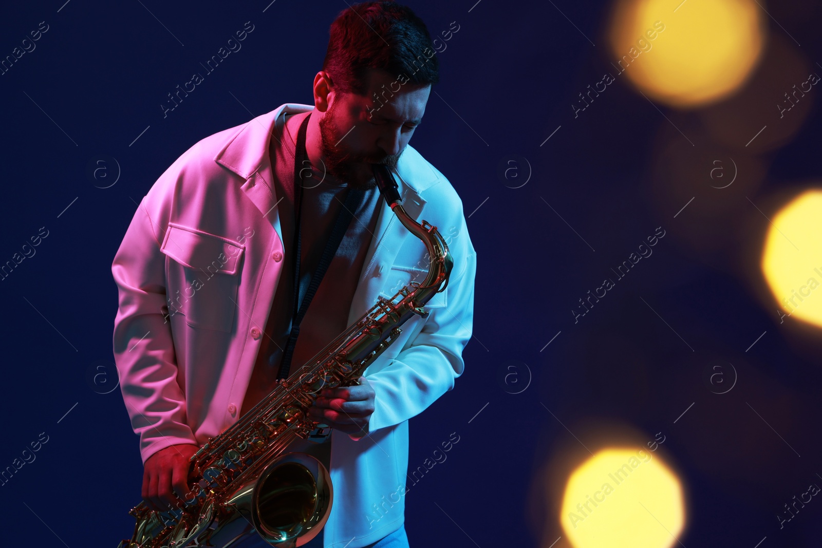 Photo of Professional musician playing saxophone on blue background with blurred lights. Bokeh effect