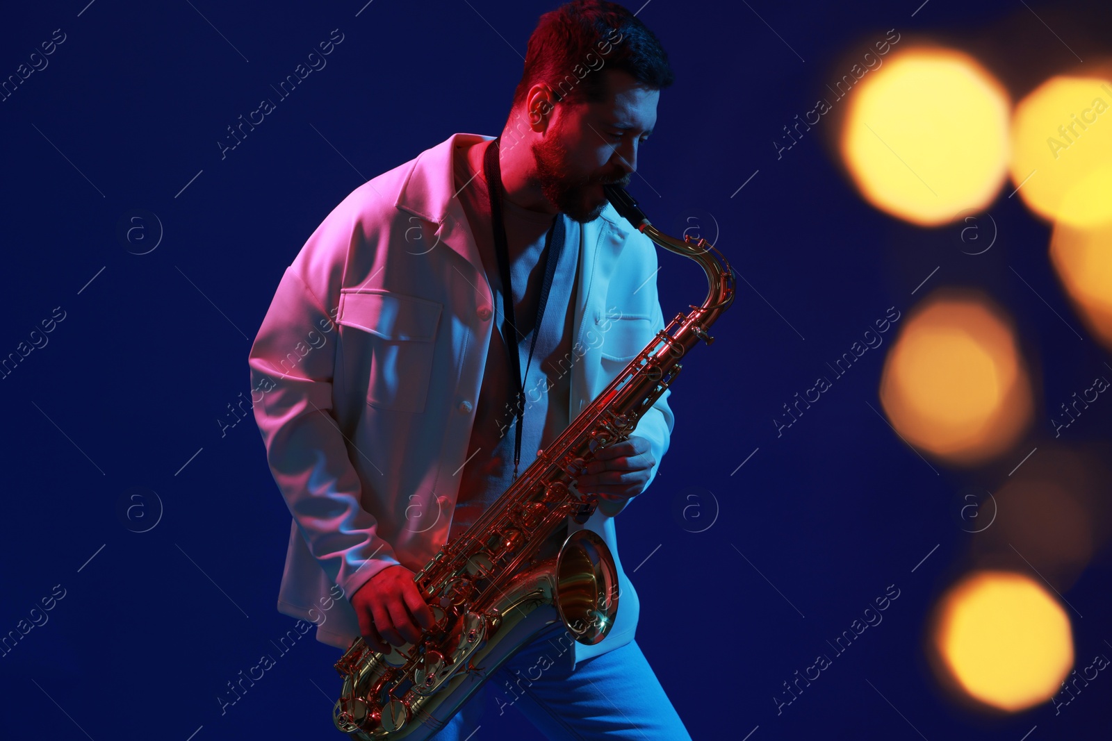 Photo of Professional musician playing saxophone on blue background with blurred lights. Bokeh effect